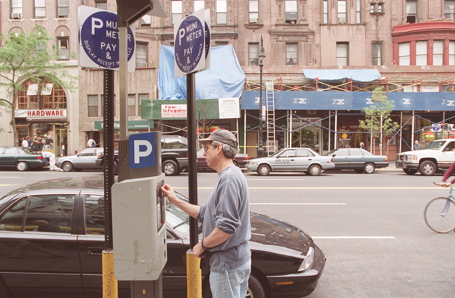 2026-06-10 ¡00parking-timeline-90s-kjtp-superJumbo.jpgA man inserts something into a device on a pole near signs that say