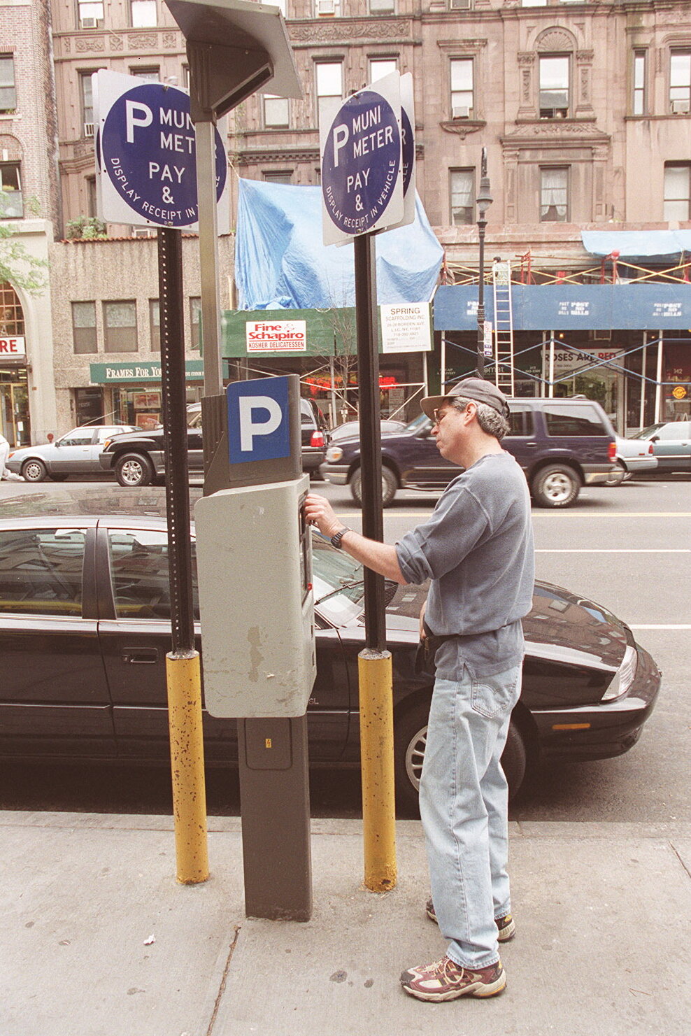 2026-06-10 ¡00parking-timeline-90s-mwjb-superJumbo.jpgA man inserts something into a device on a pole near signs that say