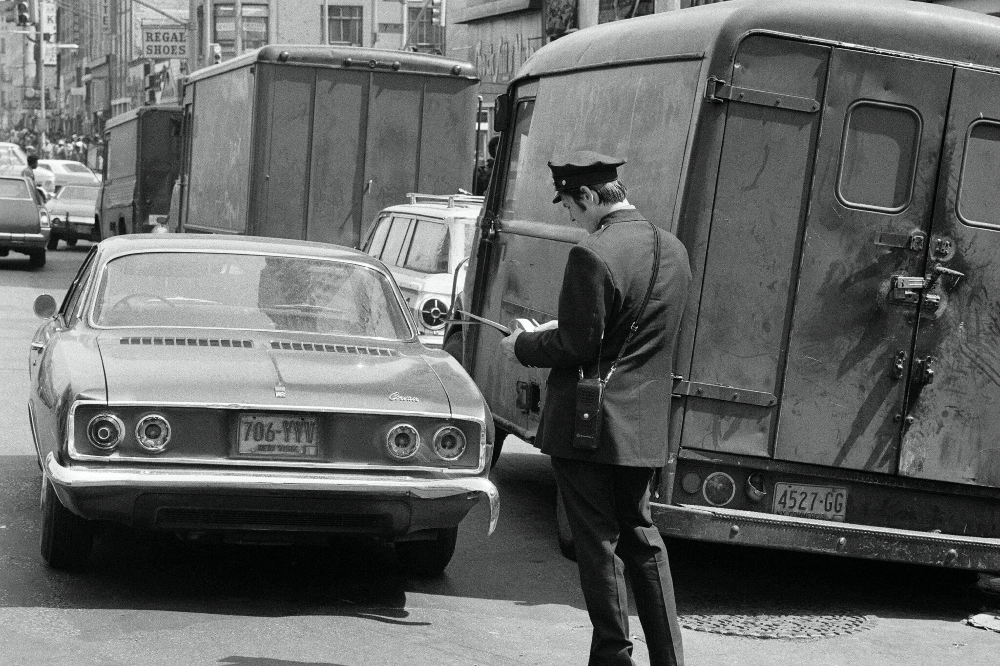2026-06-10 ¡00parking-timeline-ticket-cgjw-superJumbo.jpgA man in a uniform with his back to the camera stands near a double-parked car.