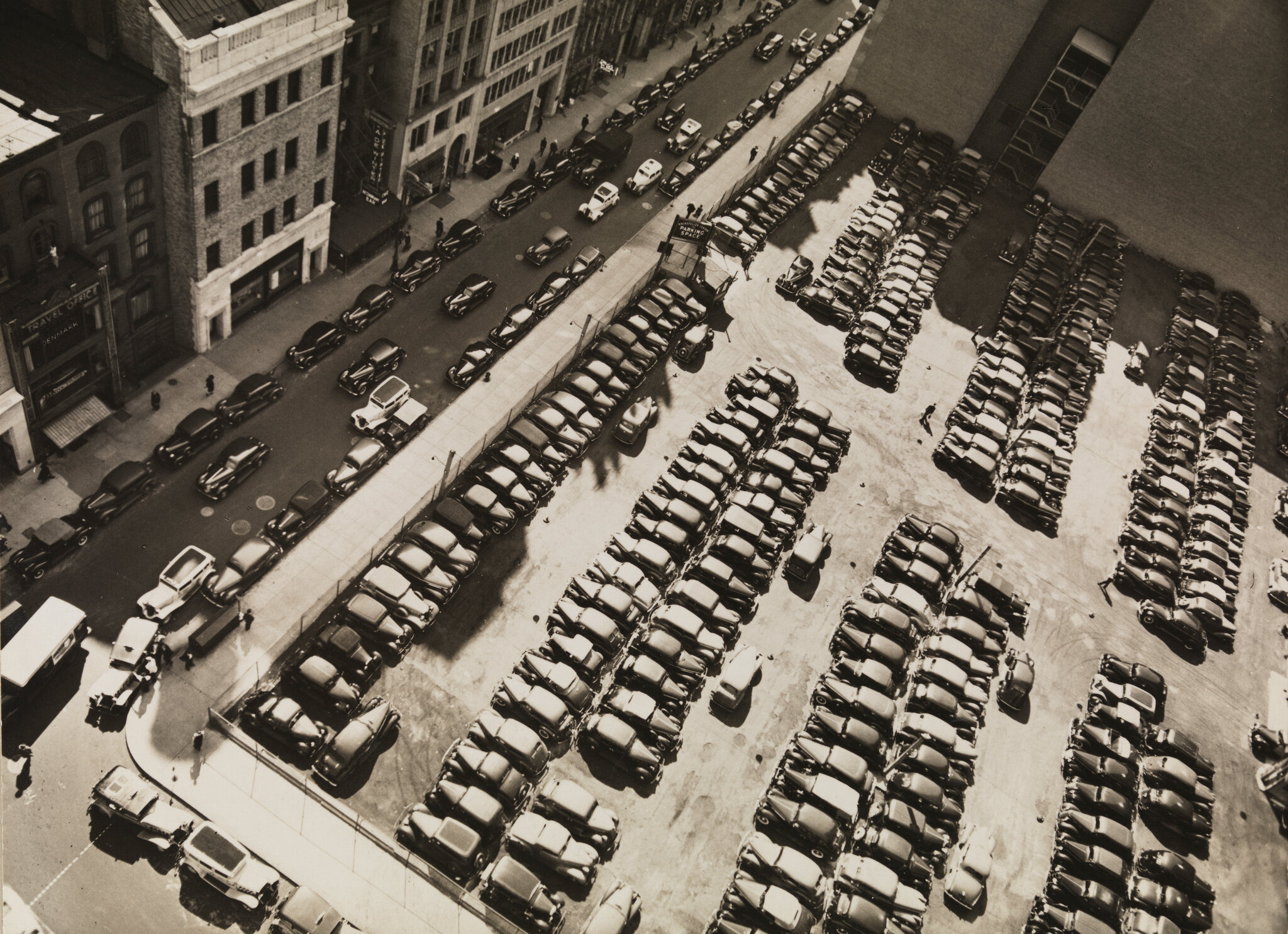 2026-06-10 ¡parking-timeline-04-fgwb-superJumbo-v2.jpgA sepia-toned black-and-white photo from 1938 of a parking lot filled with cars, as seen from above.