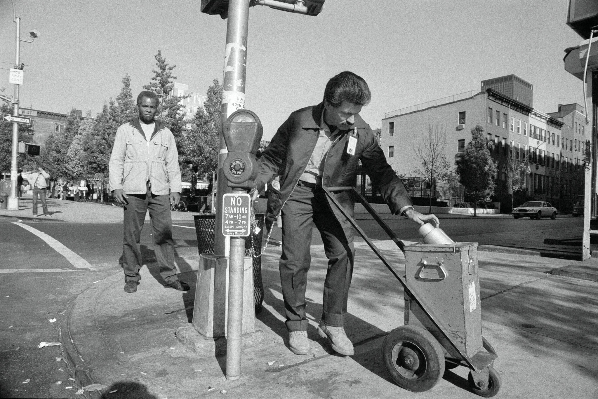 2026-06-10 ¡parking-timeline-09-fplg-superJumbo.jpgA man pushes a metal cart past a parking meter as another man looks on.