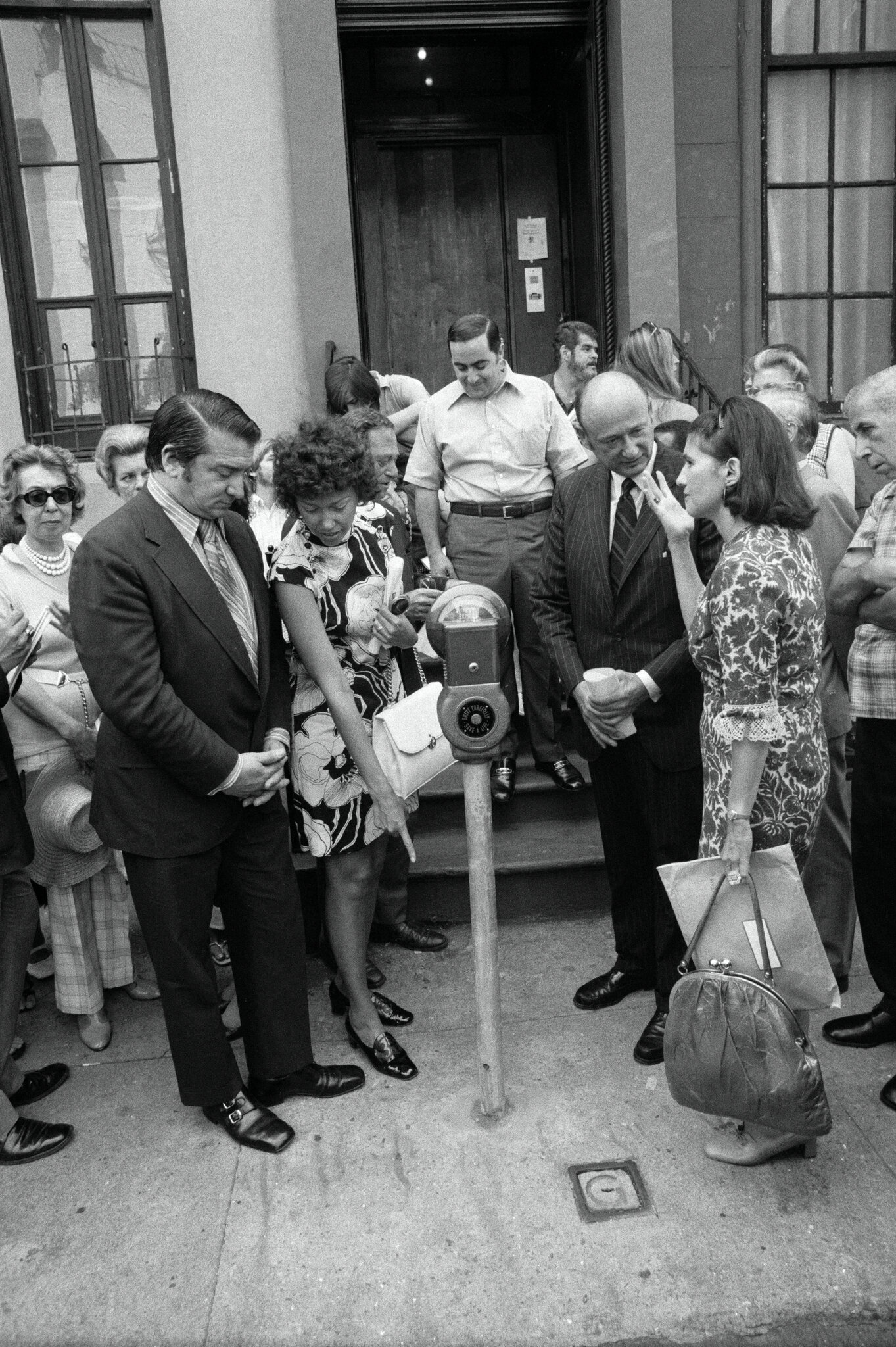 2026-06-10 ¡parking-timeline-pbtj-superJumbo.jpgPeople crowd around a parking meter that has been installed on a sidewalk. A woman points to the base of it.