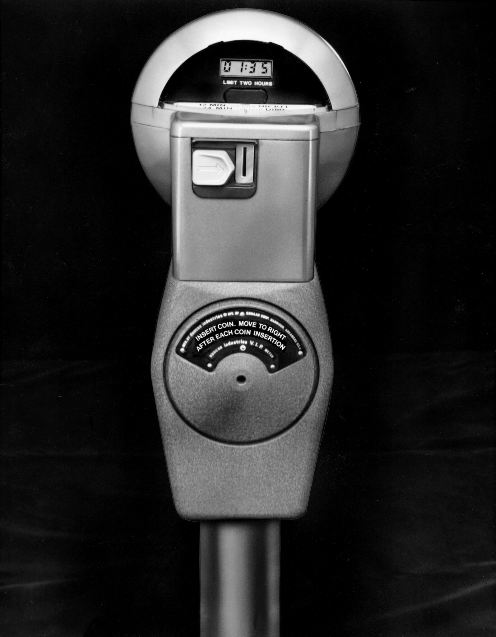 2026-06-10 ¡parking-timeline-pclj-superJumbo.jpgA black-and-white photo of a parking meter with a digital readout against a black background.