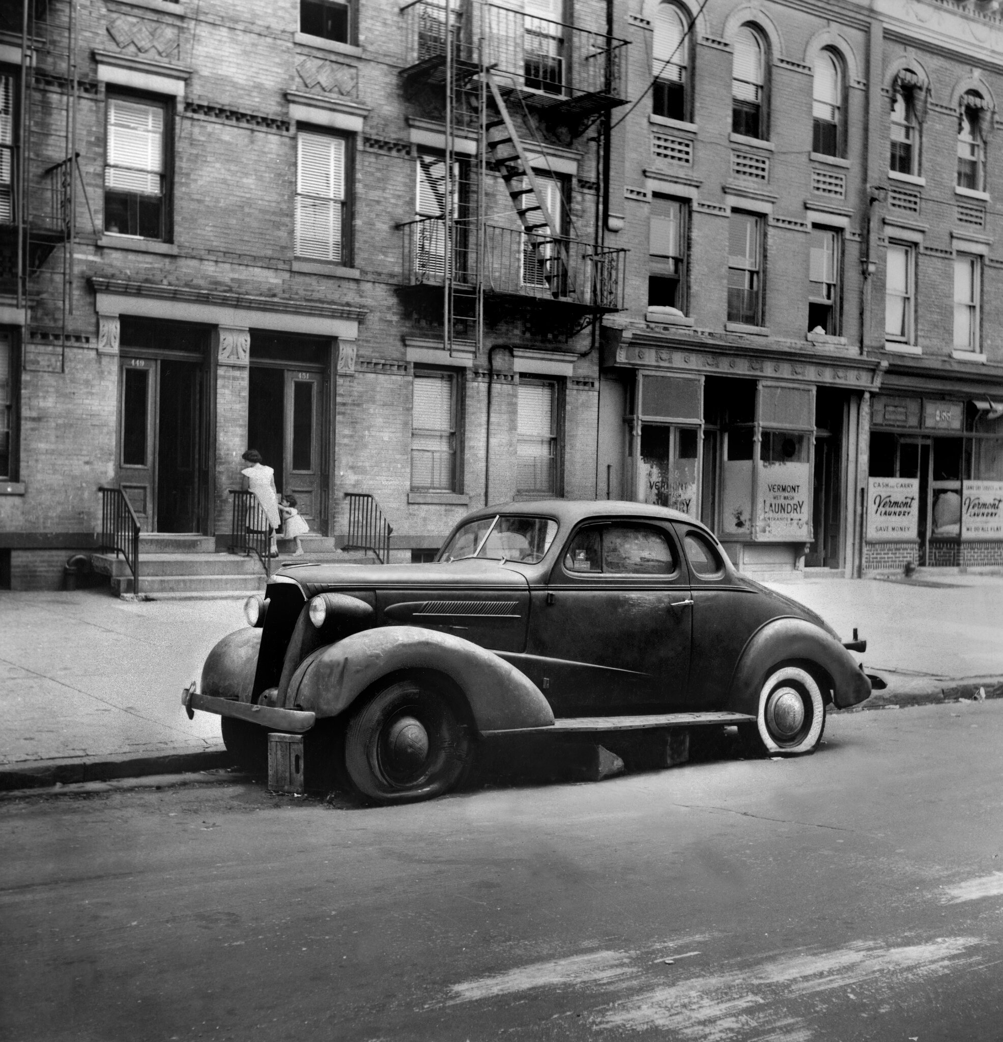 2026-06-10 ¡parking-timeline-tpmz-superJumbo.jpgA black-and-white photo from 1954 of a car from the 1930s with two flat tires parked on a city street.